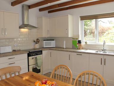 A kitchen with wooden chairs a fruit bowl on a wooden table a stove microwave and a window at Bandol in Braithwaite