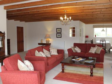 A living room with red sofas and armchairs around a wooden coffee table under wooden ceiling beams at Bandol in Braithwaite