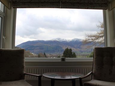 A seating area with two armchairs and a round wooden table in front of a large window showing a view of snow-capped mountains