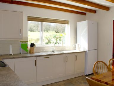 A kitchen with white cabinets a sink a window overlooking a garden a white refrigerator and wooden chairs at Bandol in Braithwaite