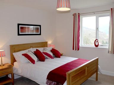 A bedroom with a wooden bed with red and white bedding red and white striped curtains and a window with a view at Bandol in Braithwaite
