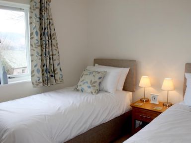 A bedroom with two single beds a wooden nightstand with two lamps and a window with patterned curtains at Bandol in Braithwaite