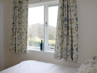 A bedroom window with patterned curtains blue and white vases on the sill and a bed with a patterned pillow at Bandol in Braithwaite