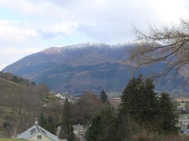 A village with houses and trees in front of mountains with snow at the top at Bandol in Braithwaite