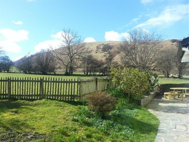 A garden with grass shrubs a wooden fence and a picnic table with hills and trees in the background at Bandol in Braithwaite