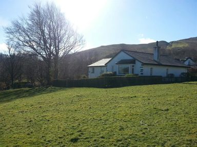 A single story house with a chimney and surrounding lawn near hills at Bandol in Braithwaite