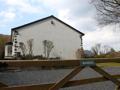 A white house with black corner stones and a wooden gate with a sign saying Bandol in Braithwaite