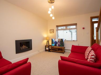 A living room with two red sofas a wall-mounted fireplace a wooden TV stand with a television and a window at Gable End in Braithwaite