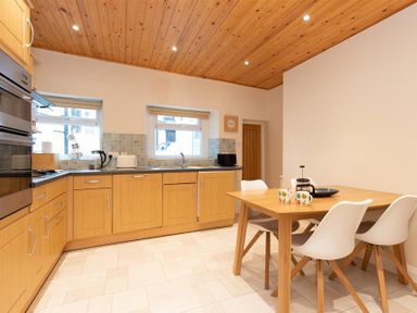 A kitchen with wooden cabinets a dining table with four chairs and kitchen appliances at Gable End in Braithwaite