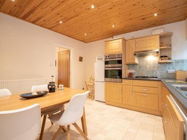 A kitchen with wooden cabinets a wooden dining table and white chairs at Gable End in Braithwaite