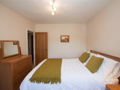 A bedroom with a bed with green cushions and throw a wooden dresser with a mirror and a wooden door in the background at Gable End in Braithwaite