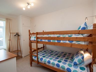 A bedroom with a bunk bed patterned bedding wooden clothes rack and window at Gable End in Braithwaite