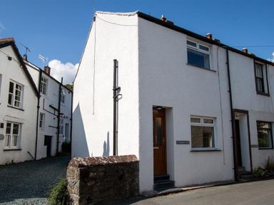 A white end terrace house with a wooden door and two windows on a street with other similar houses at Gable End in Braithwaite