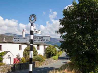 A road with a black and white striped signpost showing directions to Keswick Whinlatter Pass Lorton Newlands Buttermere in Braithwaite