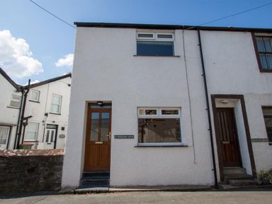 A white two-story terraced house with brown wooden doors and windows on a street at Gable End in Braithwaite