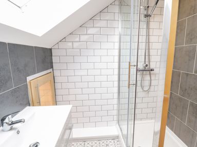 A bathroom with a white sink and chrome faucet a glass shower enclosure and tiled walls at Meadow View in Tyn-y-Gongl near Benllech