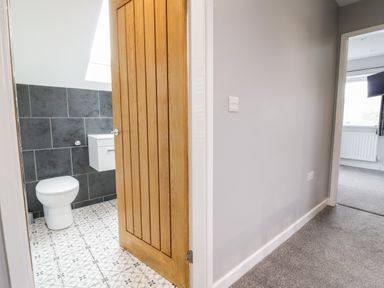 A hallway with a wooden door leading to a bathroom with a toilet and wall-mounted sink at Meadow View in Tyn-y-Gongl near Benllech