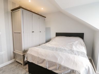 A bedroom with a bed and a wardrobe under a slanted ceiling at Meadow View in Tyn-y-Gongl near Benllech