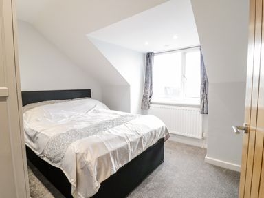 A bedroom with a bed and window under sloped ceiling at Meadow View in Tyn-y-Gongl near Benllech