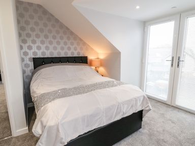 A bedroom with a double bed a bedside lamp and double glass doors at Meadow View in Tyn-y-Gongl near Benllech