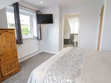 A bedroom with a bed a wooden wardrobe a window with curtains and a wall-mounted TV at Meadow View in Tyn-y-Gongl near Benllech