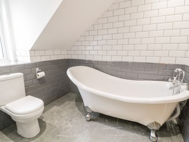 A bathroom with a freestanding bathtub and a toilet with tiled walls at Meadow View in Tyn-y-Gongl near Benllech