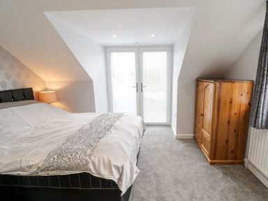 A bedroom with a bed a bedside lamp wooden wardrobe and glass doors with blinds at Meadow View in Tyn-y-Gongl near Benllech
