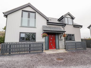 Front view of a modern house with a red door and gray fencing at Meadow View in Tyn-y-Gongl near Benllech