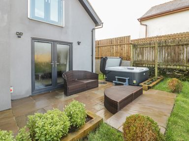 Outdoor patio with wicker furniture and a hot tub by a fenced garden at Meadow View in Tyn-y-Gongl near Benllech