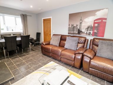 A living room with brown leather sofas a glass coffee table and a dining table with black chairs at Meadow View in Tyn-y-Gongl near Benllech