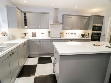 A kitchen with grey cabinets a white countertop and black and white checkered floor at Meadow View in Tyn-y-Gongl near Benllech