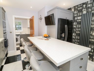 A kitchen with a white countertop island and three gray chairs by a black refrigerator and patterned wall at Meadow View in Tyn-y-Gongl near Benllech