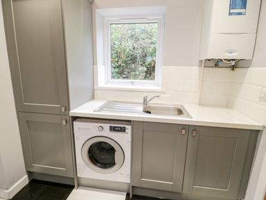 A utility room with a washing machine under a countertop and a sink above at Meadow View in Tyn-y-Gongl near Benllech