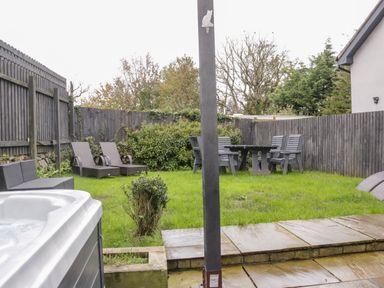 A garden with lawn chairs a table and chairs a hot tub and wooden fencing at Meadow View in Tyn-y-Gongl near Benllech