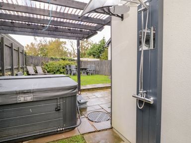 An outdoor shower next to a covered hot tub with patio furniture and grass in the background at Meadow View in Tyn-y-Gongl near Benllech