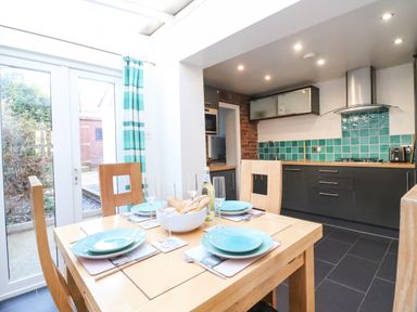 A kitchen with dining table set with plates and glasses and large glass doors with curtains at South Harbour Cottage in Weymouth