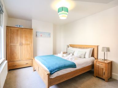 A bedroom with a wooden bed with pillows and a blue blanket two wooden bedside tables with lamps and a wooden wardrobe at South Harbour Cottage in Weymouth