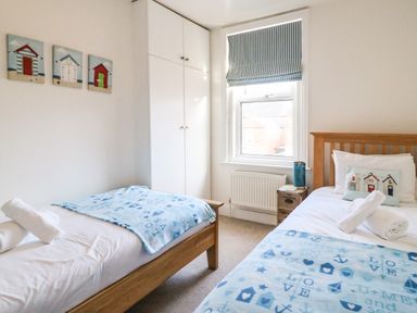 A bedroom with two single beds blue patterned blankets a window with striped blind and white built in wardrobe at South Harbour Cottage in Weymouth