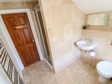 A tiled bathroom with a wooden door a shower a wall-mounted sink mirror and toilet at South Harbour Cottage in Weymouth