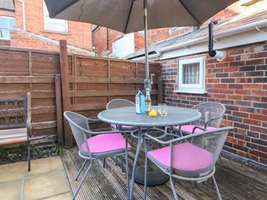 An outdoor patio with a round metal table and four chairs with pink cushions under a large umbrella at South Harbour Cottage in Weymouth