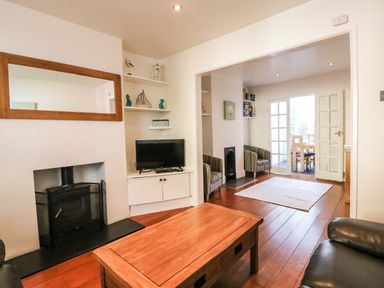 A living room with a wood stove coffee table television and armchairs leading to a dining area at South Harbour Cottage in Weymouth