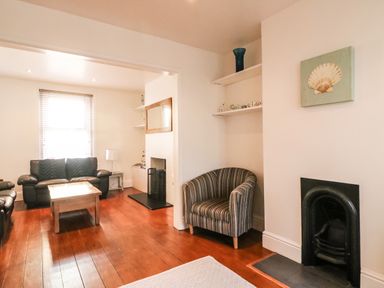 A living room with sofas a wooden coffee table a striped armchair and a fireplace at South Harbour Cottage in Weymouth