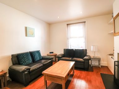 A living room with two black sofas a wooden coffee table and a window at South Harbour Cottage in Weymouth