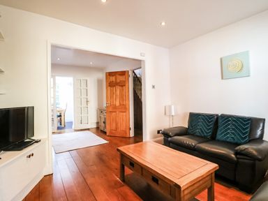 A living room with a black leather sofa with two cushions a wooden coffee table a television on a cabinet and a wooden door opened at South Harbour Cottage in Weymouth