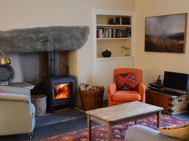 A living room with a wood burning stove an orange armchair a wooden coffee table and a striped armchair at Thomas Cottage in Hartsop