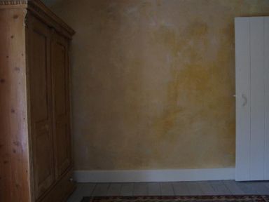 A wooden wardrobe against a textured wall next to a white door on a wooden floor