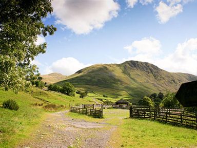 A rural path with fenced enclosures and hills in the background at Thomas Cottage in Hartsop