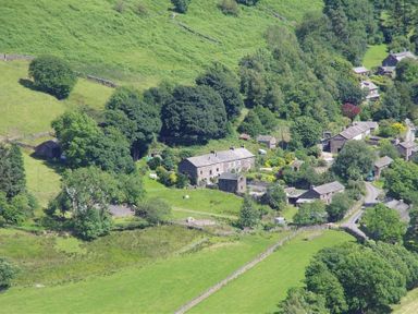 A rural village with stone houses surrounded by green fields and trees at Thomas Cottage in Hartsop