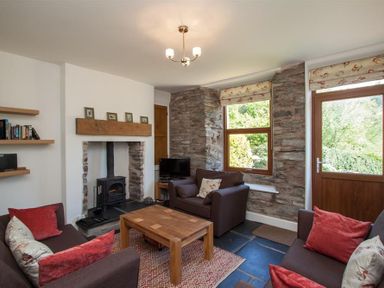 A living room with brown sofas a wooden coffee table a small fireplace and stone wall at Robins Nest in Coniston