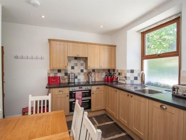A kitchen with wooden cabinets black countertops a stainless steel sink and window and a wooden dining table with white chairs at Robins Nest in Coniston